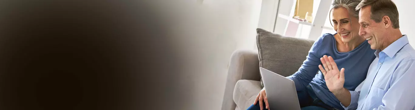 Casal realiza consulta médica online no notebook e sorriem, sentados em um sofá.