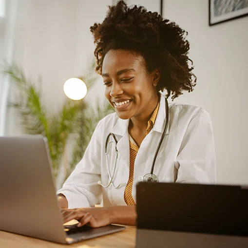 Médica feliz, sorridente, atendendo e utilizando um computador