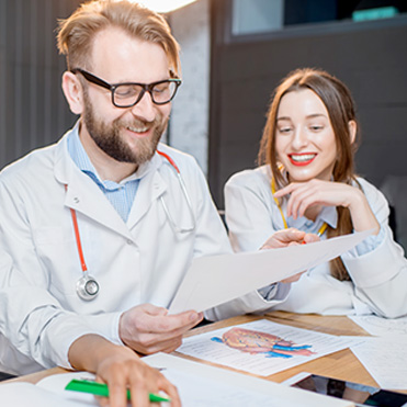 Médico sorrindo segurando papel e mostrando conteúdo à colega de trabalho