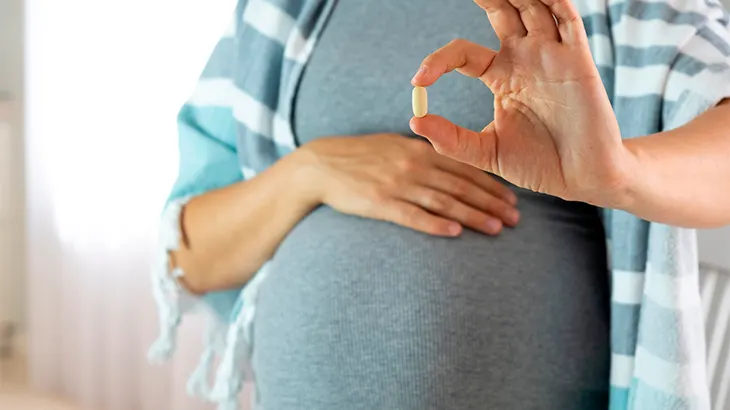 Mulher segurando uma cápsula e com a outra mão na barriga