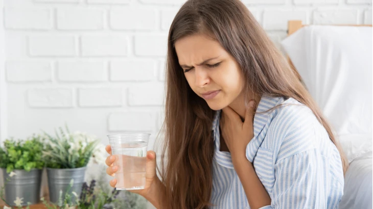 Mulher com a mão no pescoço e tomando água com os olhos fechados