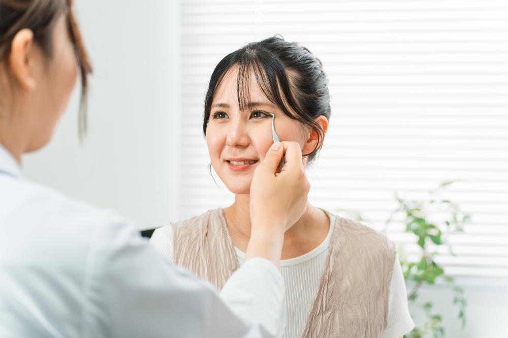 Cirurgia de palpebras. Profissional médico avaliando a região dos olhos de uma paciente, marcando a pálpebra com pinça, representando o preparo para uma blefaroplastia.